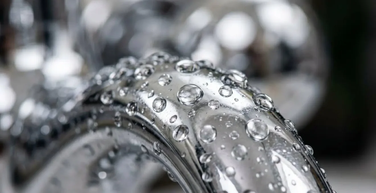 Gros plan macro sur des gouttes d'eau glissant sur une surface métallique chromée évoquant la plomberie moderne avec reflets et texture tactile